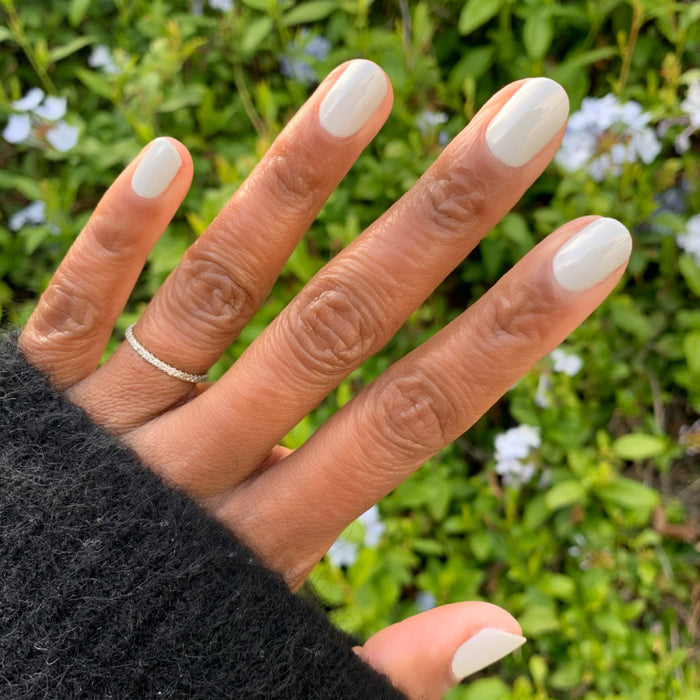 Hand with nails painted in Cloudy Skies polish showing a soft muted grey manicure in natural outdoor light