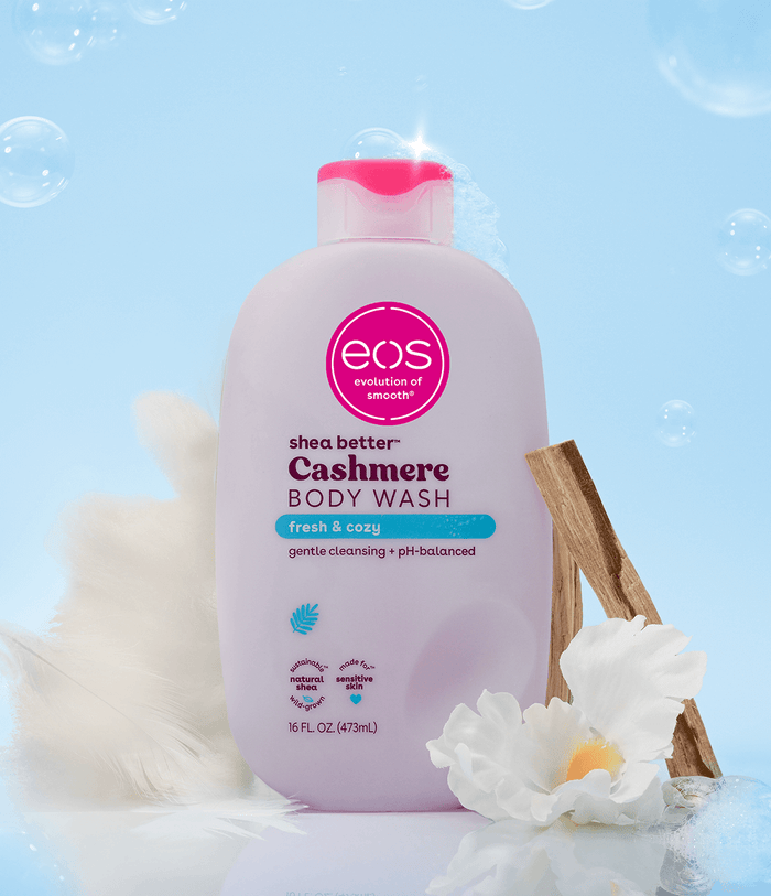 eos shea butter cashmere body wash bottle with flowers and cinnamon sticks on a light blue background