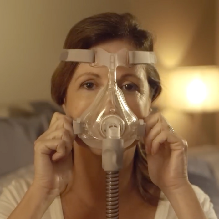 Front-facing image of a woman adjusting a Quattro™ Air Full Face Mask with Headgear For Her on her face