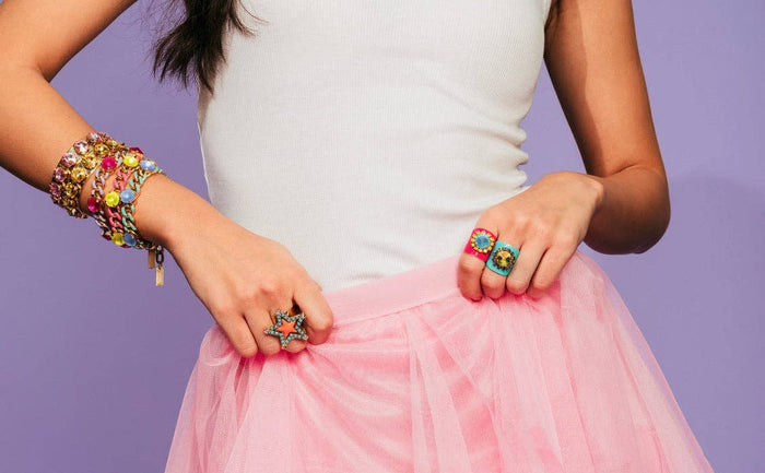 Person wearing colorful jewelry including rings and a bracelet on a purple background