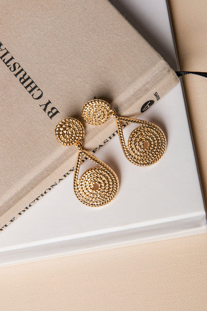 Gold earrings on a beige surface with 'By Christin' branding.