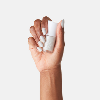 Hand holding Olive and June Cloudy Skies nail polish bottle with nails painted in soft misty grey shade.