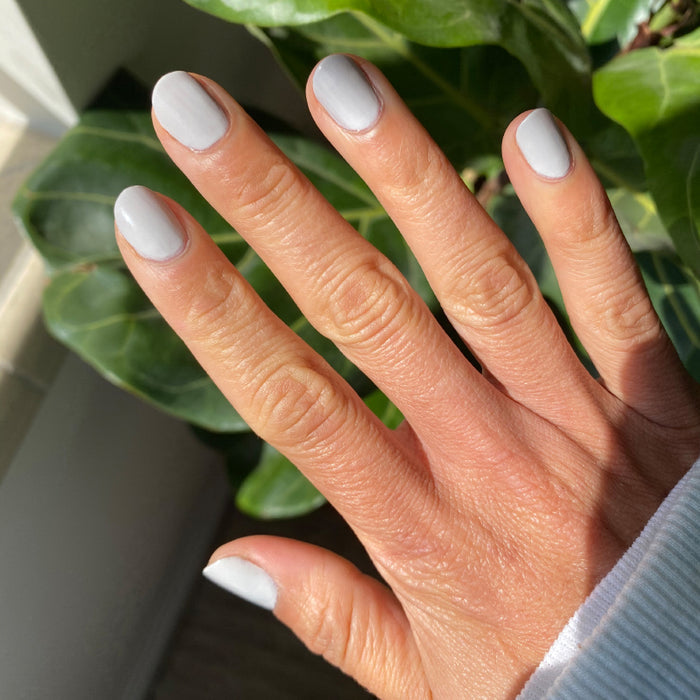 Hand with nails painted in Cloudy Skies long-lasting polish showing a soft misty grey manicure in natural light
