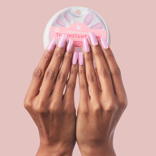 Cockatoo - Press-On | Long | Squoval long squoval false nails in glowing lavender with pink tint on hands holding round white packaging