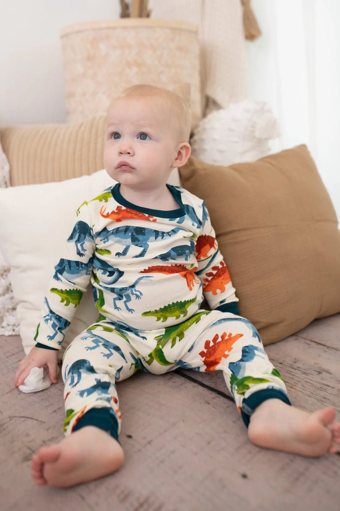 Baby sitting in Hatley Dino Park pajama set with teal trim and breathable organic cotton fabric.