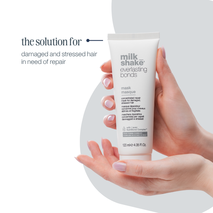 Hand holding a tube of Milk Shake Everlasting Bonds mask against a light background