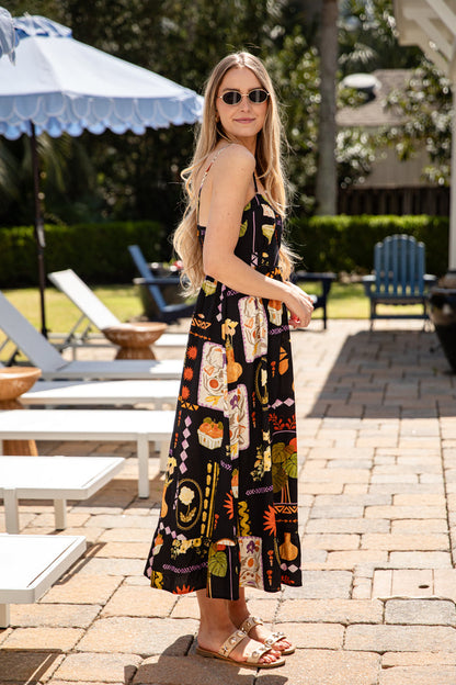 Woman in a patterned dress standing on a patio with lounge chairs and an umbrella in the background.