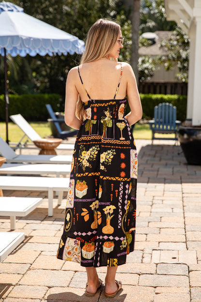 Woman wearing a patterned dress standing on a patio with outdoor furniture and greenery.