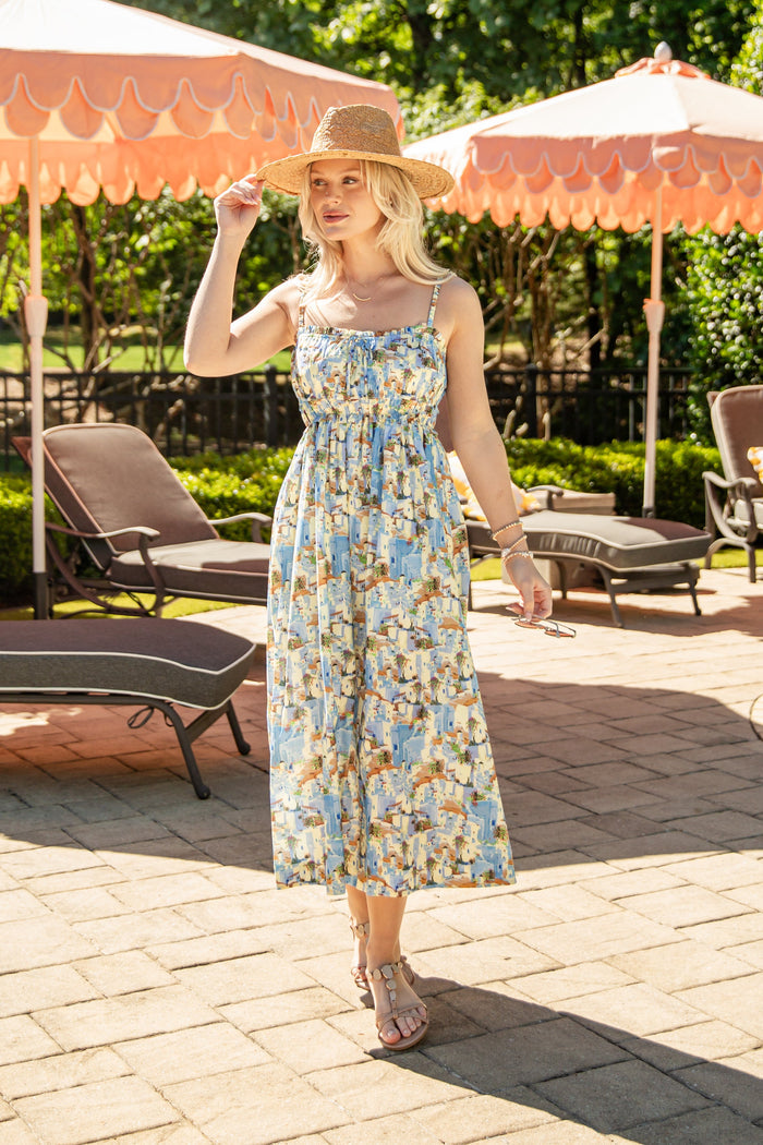 Woman in a floral dress standing on a patio with orange umbrellas and lounge chairs.