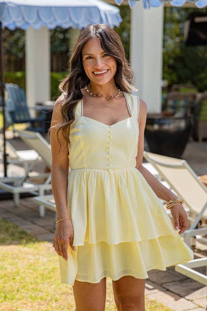 Woman in a yellow dress standing outdoors with lounge chairs and umbrellas in the background