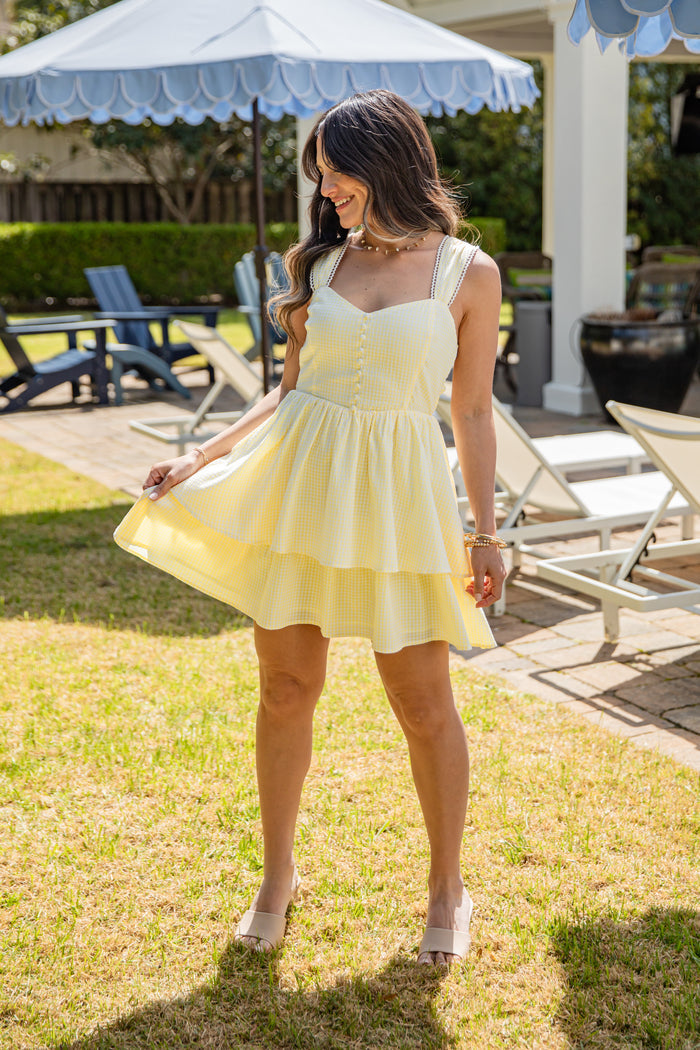 Woman in a yellow dress standing outdoors near lounge chairs and an umbrella.