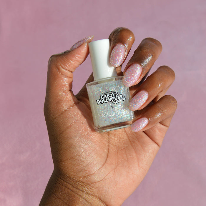 Gabby's Dollhouse silver glitter nail polish on a medium skin tone, hand holding the bottle