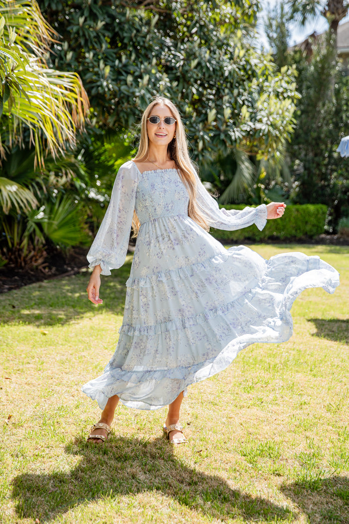 Woman in a flowing light blue dress standing on grass with trees in the background