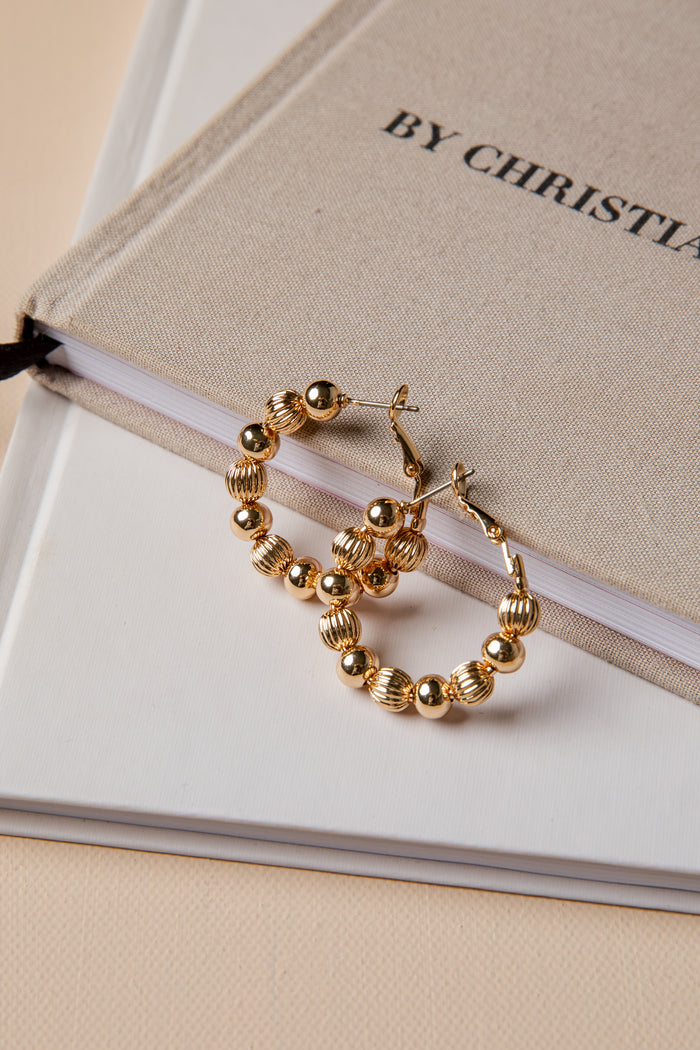 Gold hoop earrings on a book with 'By Christian Dior' text