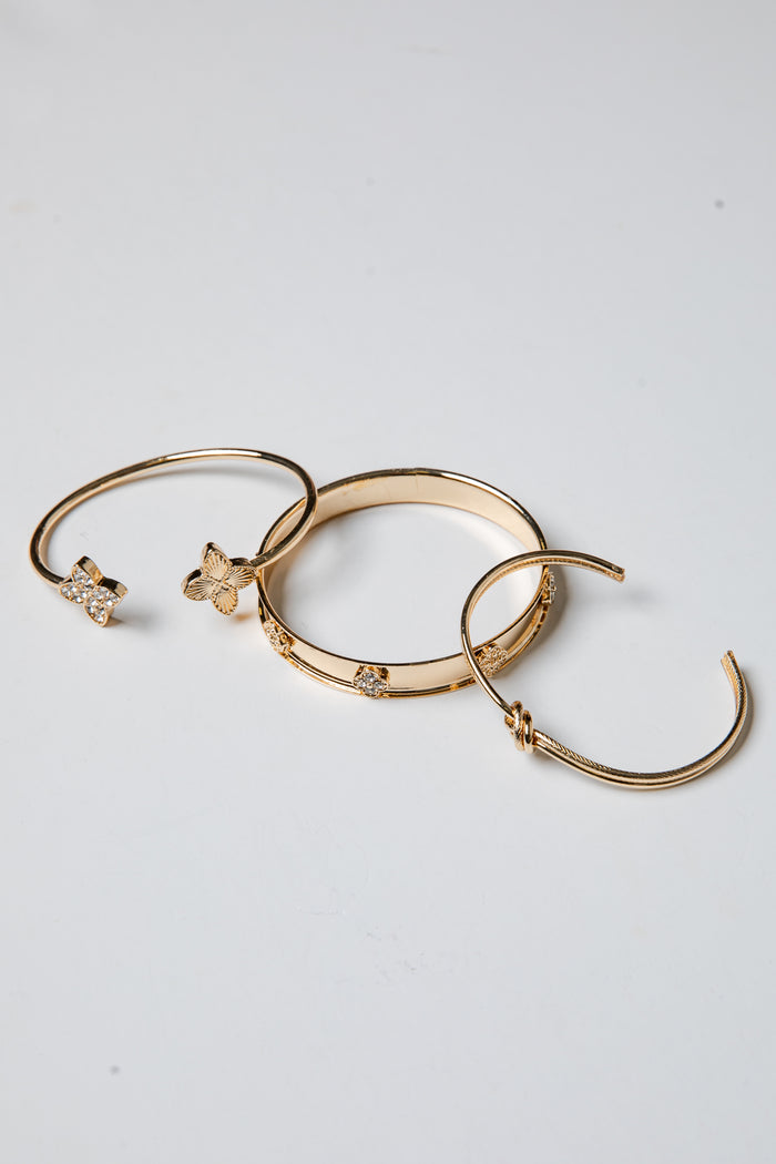 Three gold bracelets with decorative elements on a light gray background