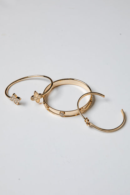 Three gold bracelets with decorative elements on a light gray background