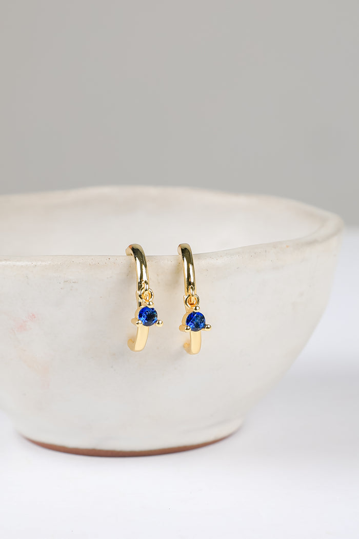 Gold earrings with blue gemstones on a white surface