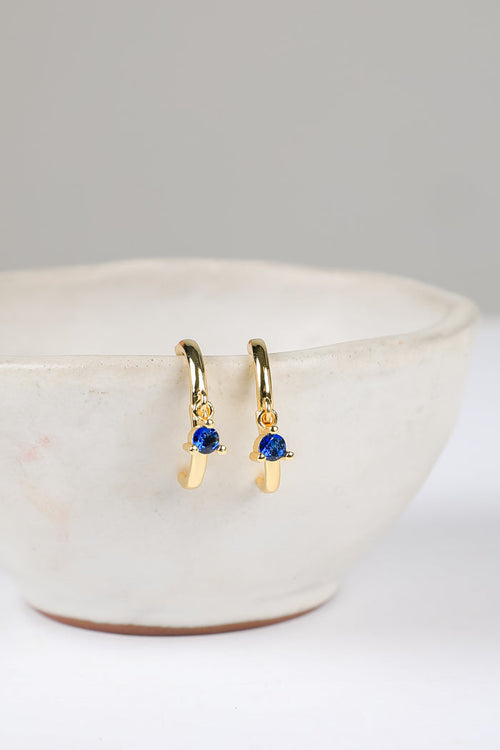 Gold earrings with blue gemstones on a white surface