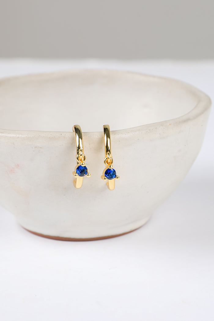 Gold earrings with blue gemstones on a white surface