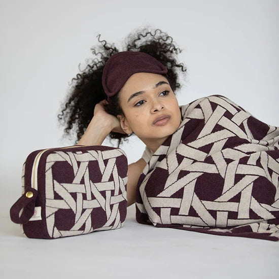 Woman wearing a patterned headband and blanket, holding a matching pouch against a white background