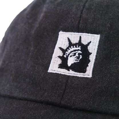 Close-up of a black Trophy Eyes Dad Hat with an embroidered patch showing a stylized black and white Statue of Liberty face.