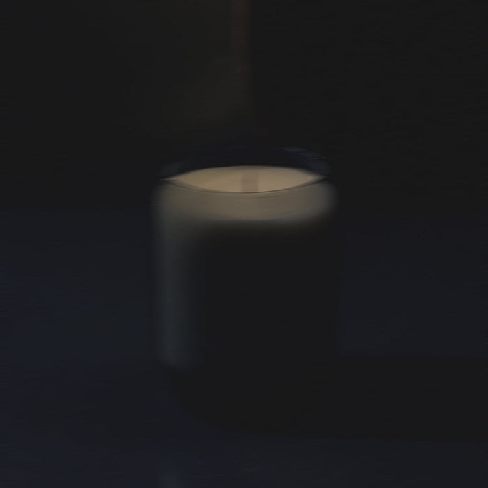 Waxed perfume candle with lit flame in glass jar, softly blurred