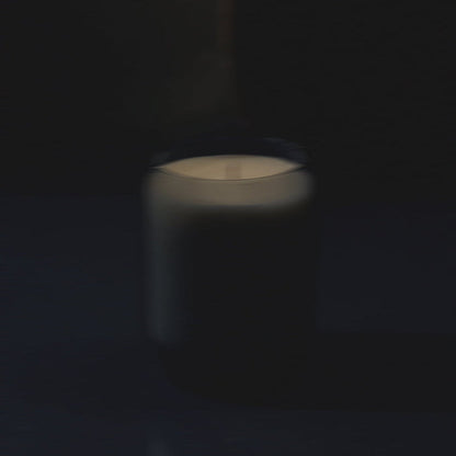 Waxed perfume candle with lit flame in glass jar, softly blurred